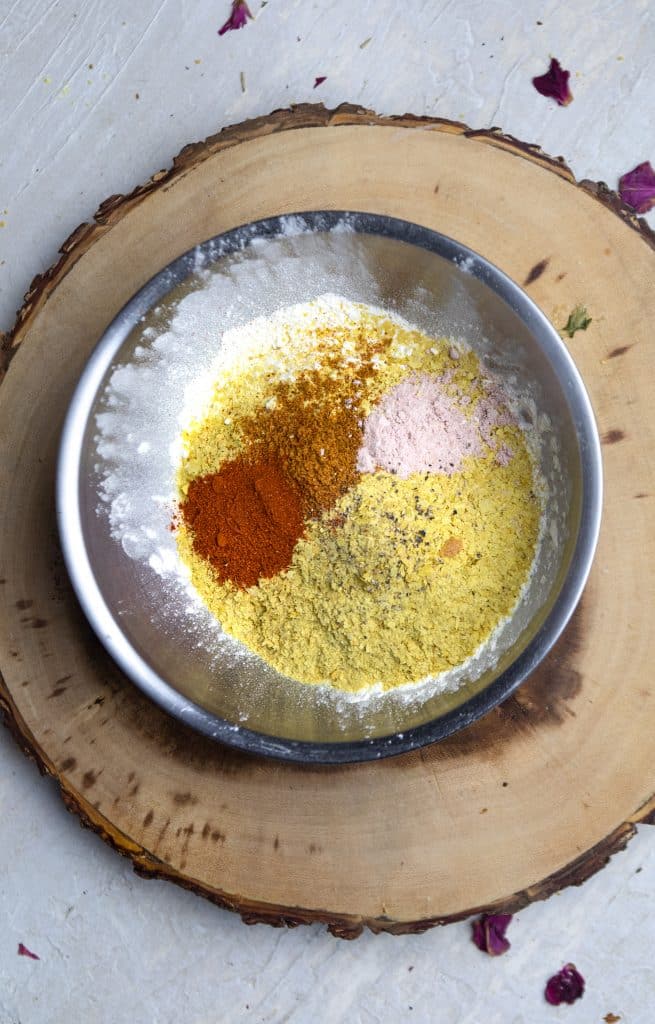 A metal bowl on a wooden board filled with flour and many different colored spices