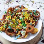 A plate of curly fries, then a layer of onion rings over the fries, then a layer of beefy crumbles, then a layer of melted plant cheddar cheese, then a layer of shredded lettuce, then a drizzle of katsup, then another drizzle of blue burger sauce