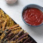 A small bowl of ketchup next to a plate of fries