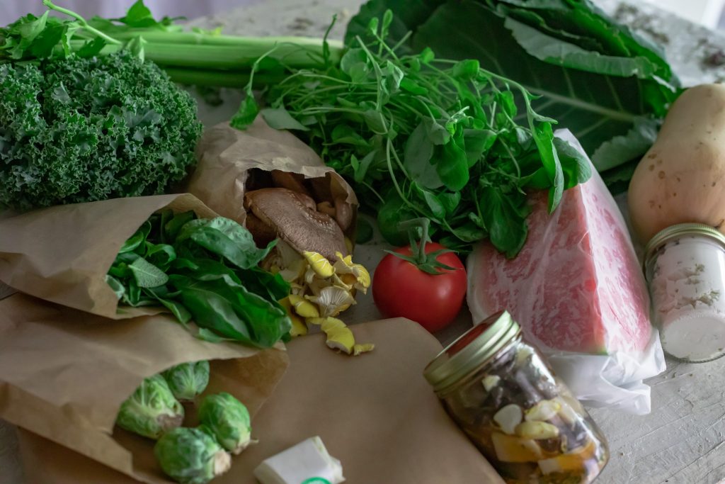 Fresh vegetables in parchment paper. Bright green kale piles on fresh basil and brussel sprouts, nuzzled next to oyster mushrooms and a bright red tomato. Watercress hugs the tomato and spills over watermelon and Collard Greens. Butternut squash lays slightly over the collard greens with a jar of white skordila below. 
This is a great example of foods that are seasonal in Colorado 