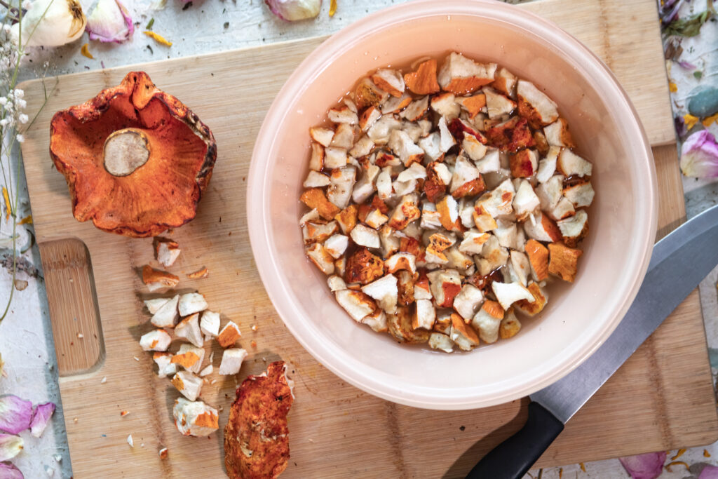 A bowl of broken up lobster mushrooms on a cutting board with more lobster mushrooms 