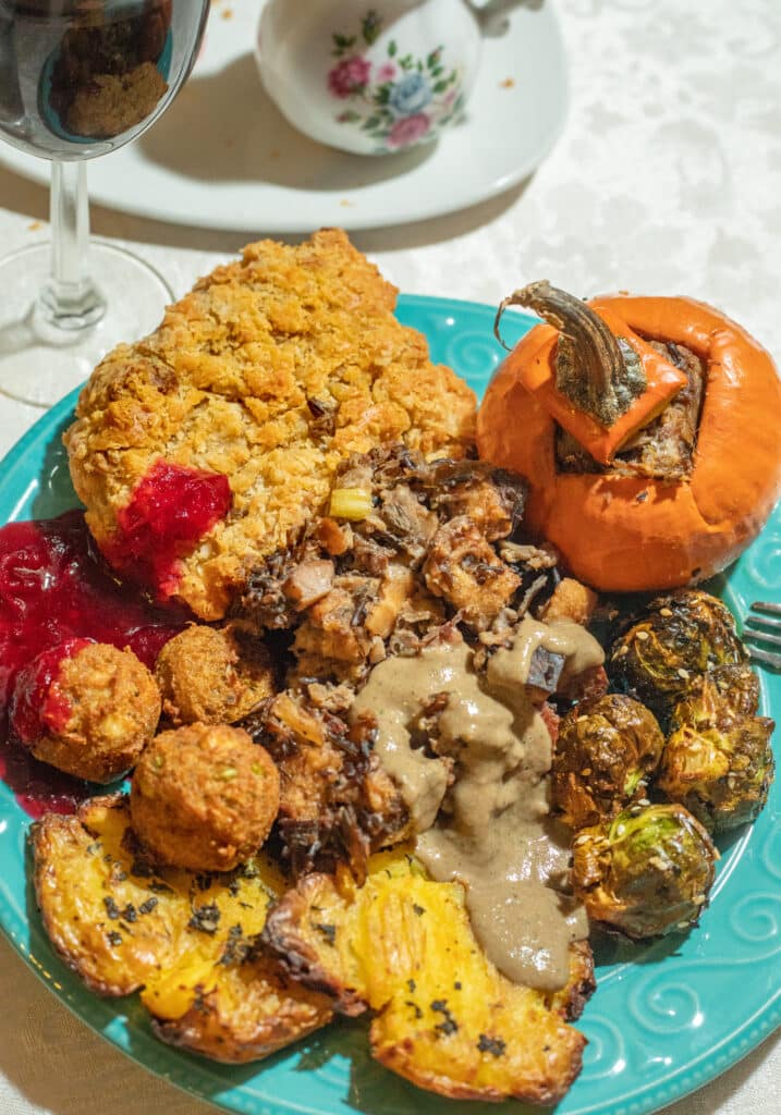 A vegan Thanksgiving plate with vegan wild rice mushroom stuffing, gravy, stuffed pumpkin, roasted brussels sprouts, seitan chicken, stuffing fritters, smashed potatoes, and cranberry sauce