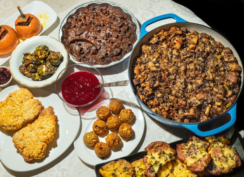 A vegan Thanksgiving spread with Wild Rice Mushroom Stuffing, pie, smashed potatoes, stuffing fritters, seitan chicken, roasted brussels sprouts, cranberry sauce, and stuffed pumpkins