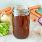 A glass jar of vegetable broth surrounded by vegetables