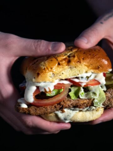 a person holding a crispy fried chicken of the woods sandwich with ranch dripping down