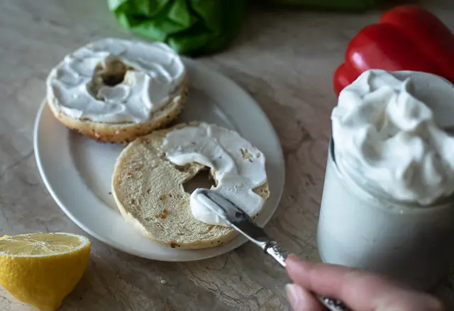 Mayo being spread over a bagel 