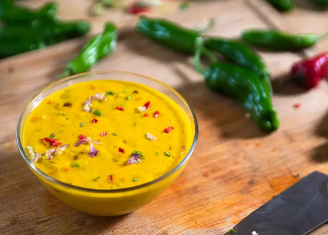 A bowl of queso with sprinkles of chopped peppers over it 