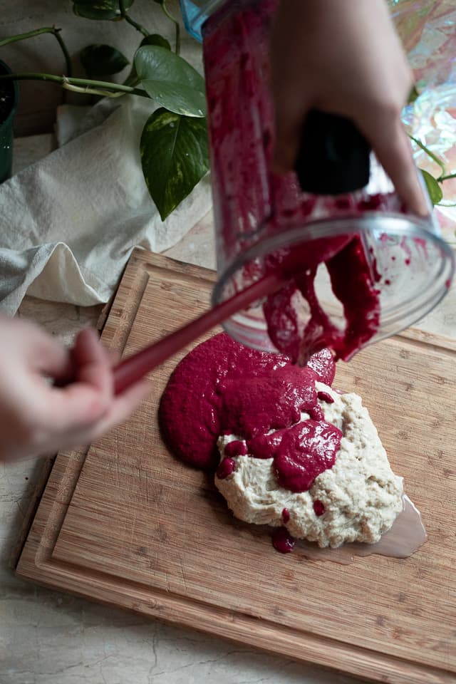 a person pouring out red batter over a wad of dough