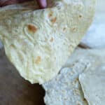 a person holding a tortilla with a stack of tortillas below