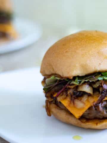a burger with cheddar cheese, caramelized onions, greens, in a bun