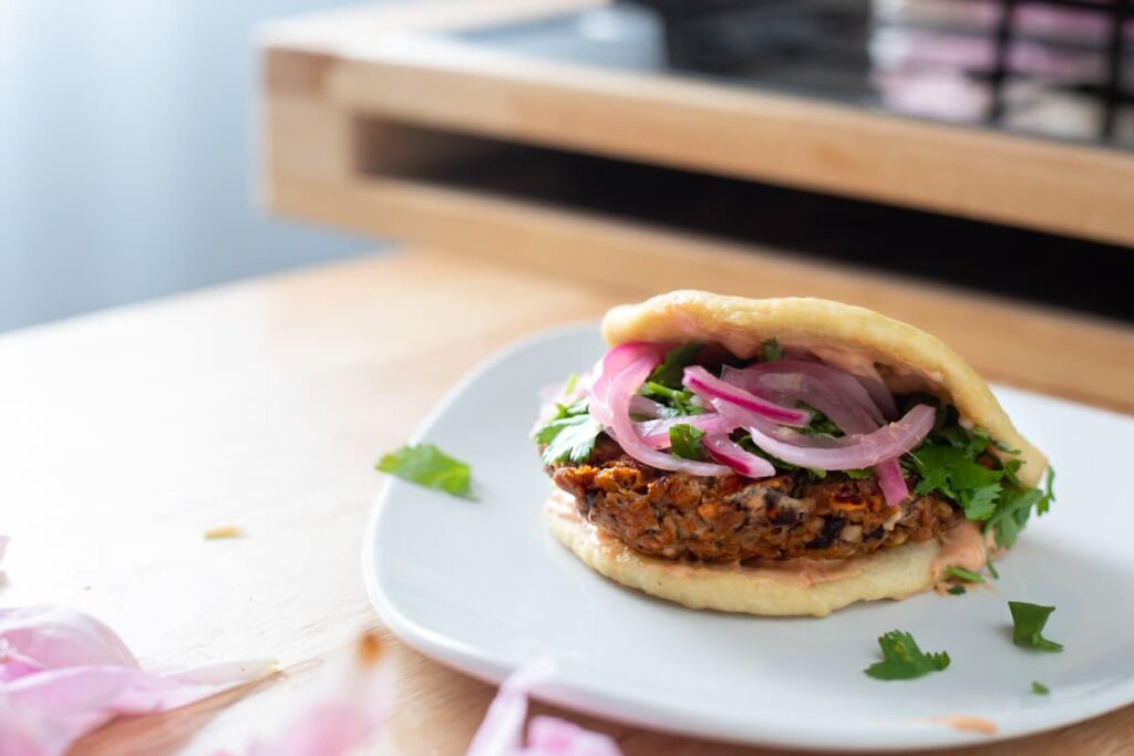 a burger inside of a bao bun topped with pickled red onion and cilantro