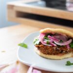 a burger inside of a bao bun topped with pickled red onion and cilantro