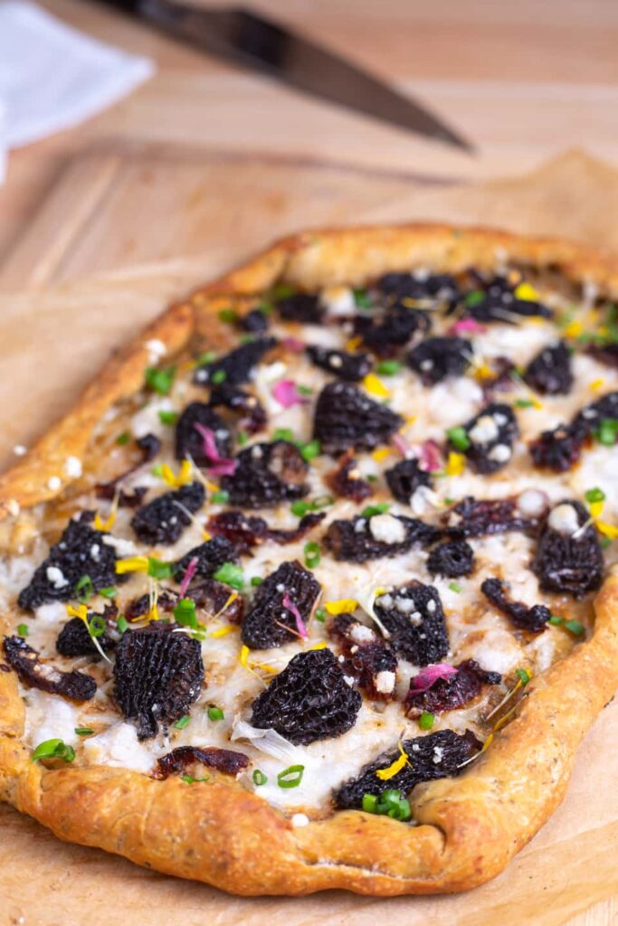 A pizza with morel mushrooms, fresh green onions, and edible flowers