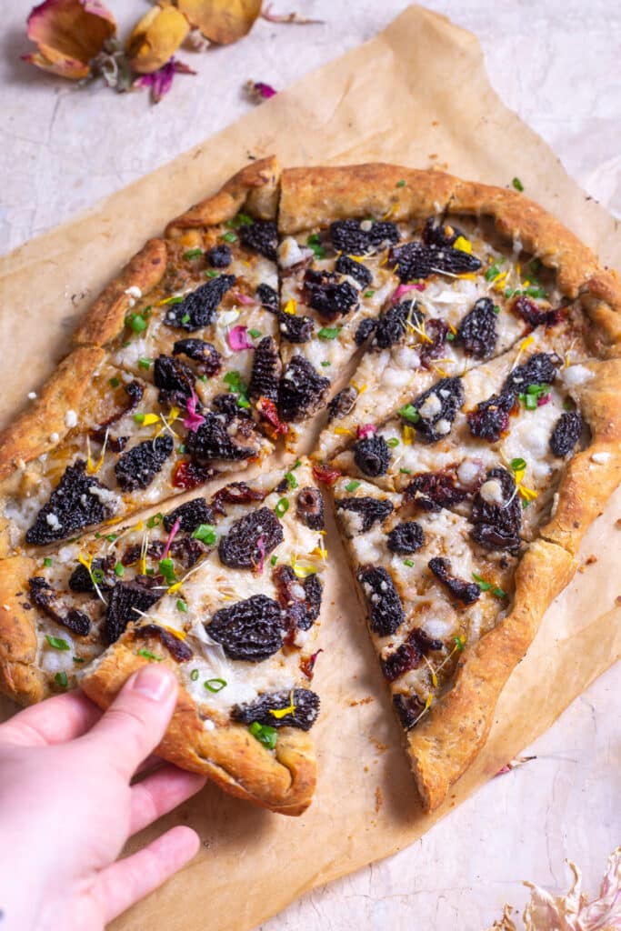 a person grabbing a slice of mushroom pizza