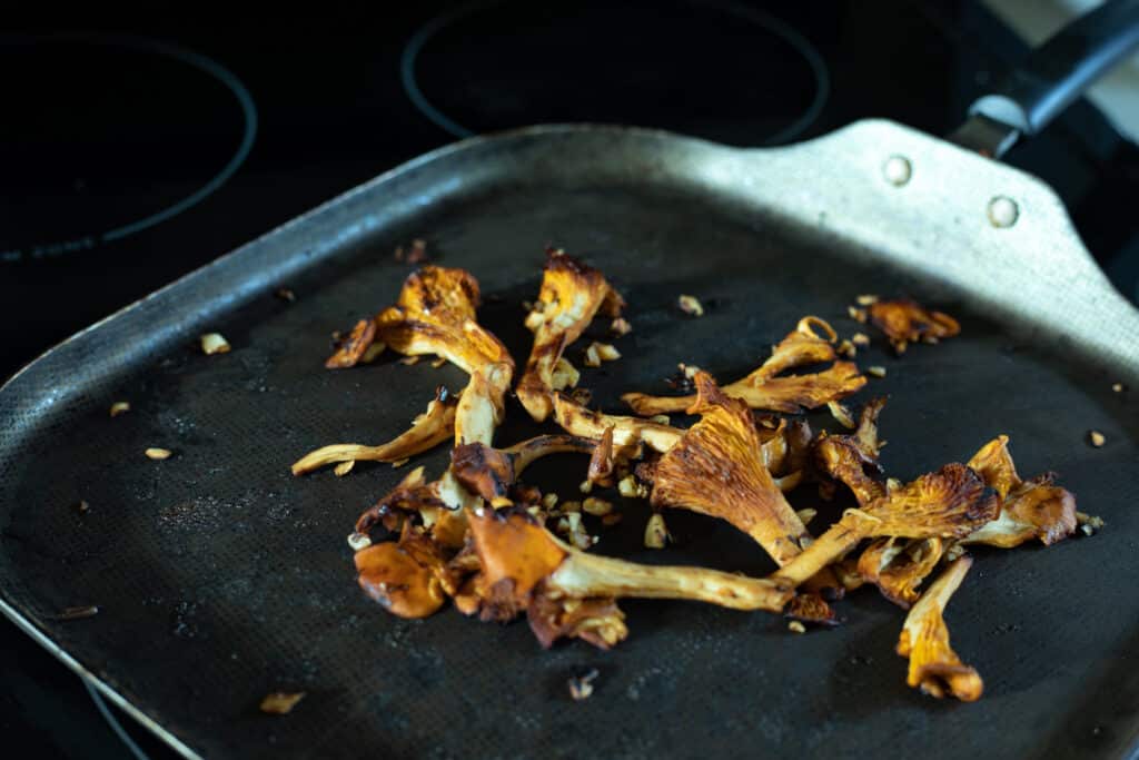 A frying pan on the stove with cooked chanterelle mushrooms and garlic