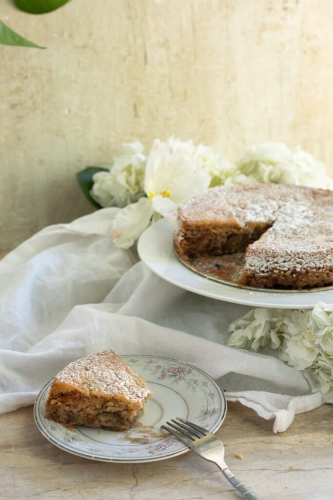 a slice of cake on a small plate next to a full cake on a cake stand