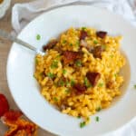 A white bowl of mac and cheese with lobster mushrooms on top sitting on a marble counter top