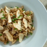 A white bowl of rice topped with sliced mushrooms and green onions