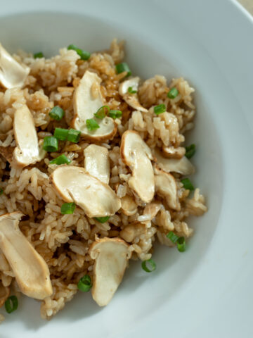 A white bowl of rice topped with sliced mushrooms and green onions