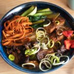 a bowl of oyster mushroom ramen loaded with toppings like carrot, bok choy, roasted mushrooms, leeks, and an edible flower