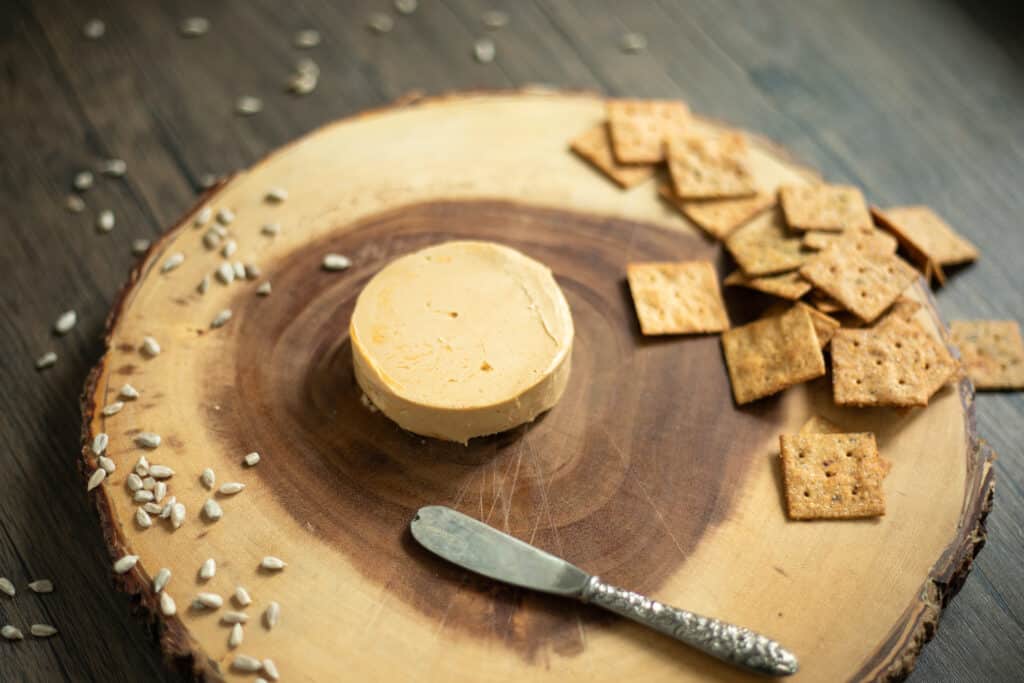 a round of cheese on a wooden cheeseboard next to crackers and a cheese knife