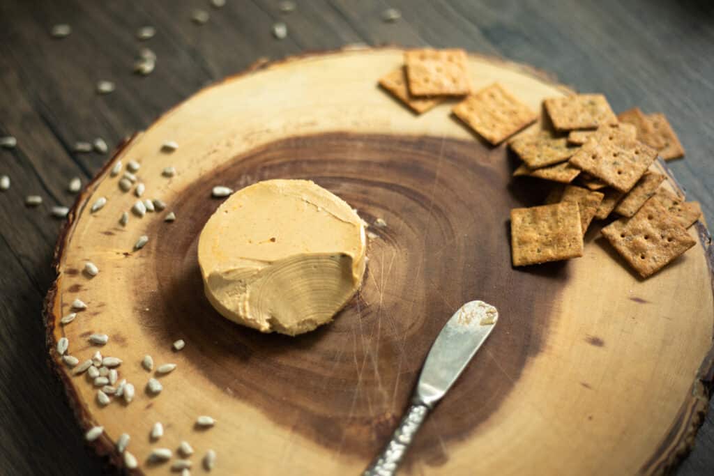 A wheel of cheese on a wooden cheese board with crackers and sunflower seeds