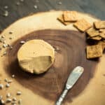 a wheel of cheese on a wooden cheeseboard with crackers and sunflower seeds