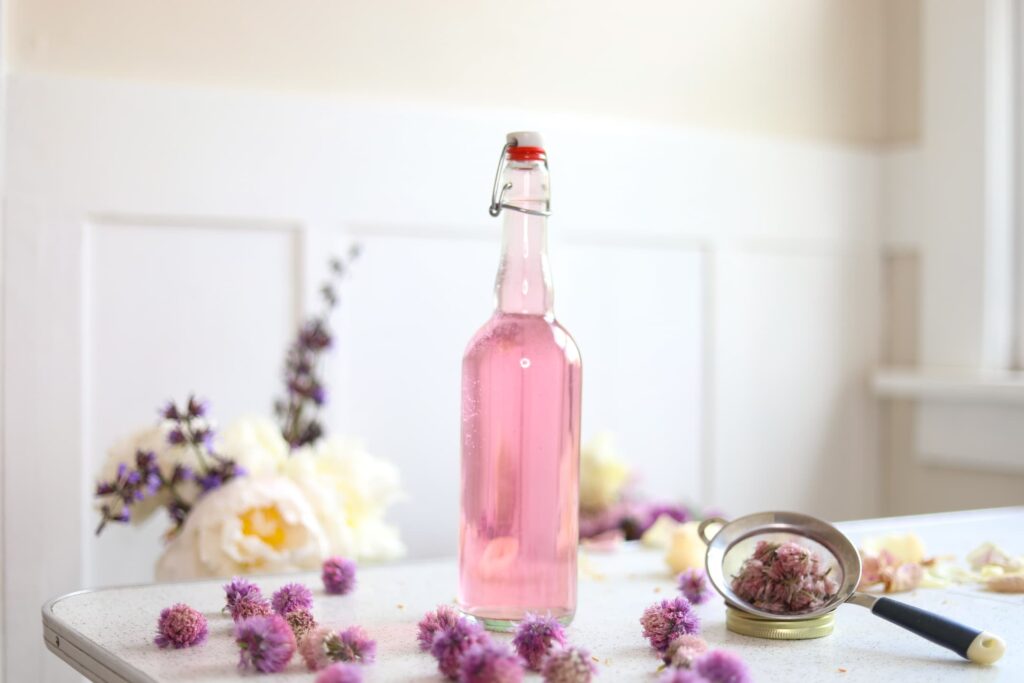 a glass jar filled with pink chive blossom vinegar on a table next to fresh chive blossoms