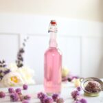 a bottle of pink chive vinegar next to fresh chive flowers on a white table