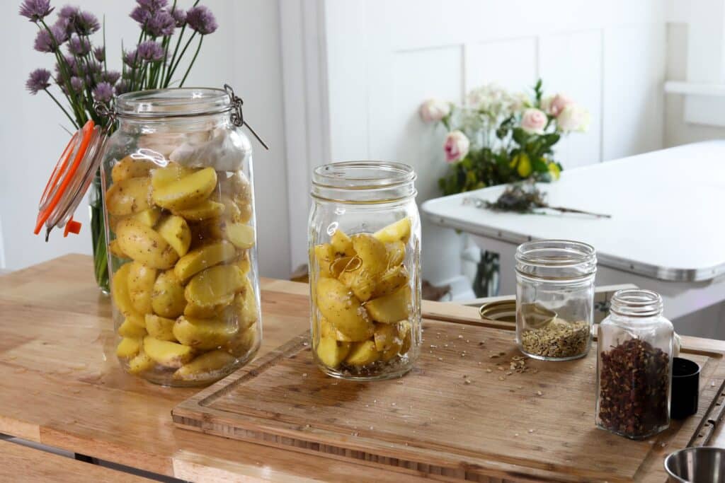 two large jars filled with cut potatoes and salt next to small jars of spices on a wooden table