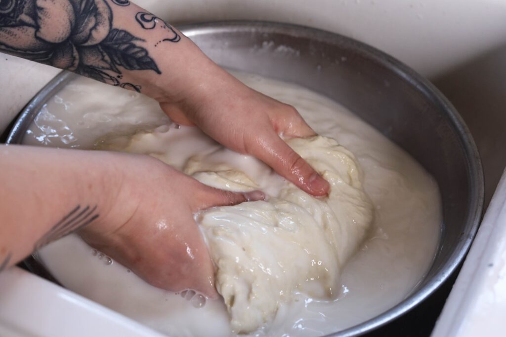 a person gripping dough in a bowl of water