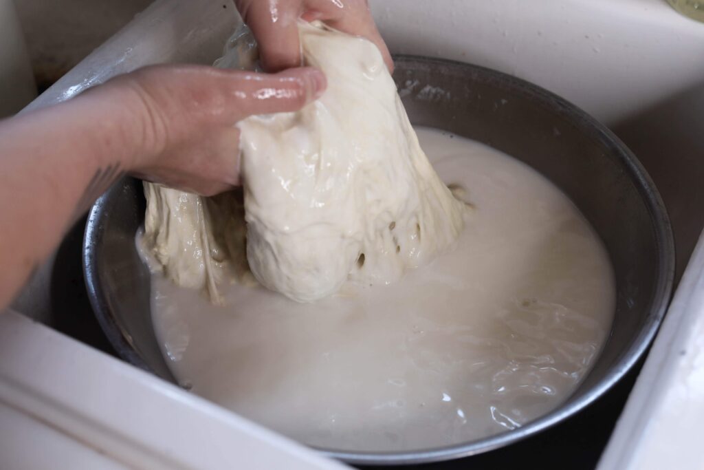 a person stretching dough in white starchy water