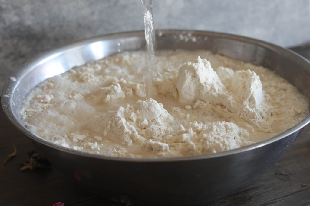 water being poured into a silver bowl filled with bread flour