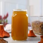 a jar filled with bright orange and yellow oil next to a lobster mushroom on a white table