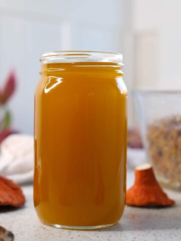 a jar filled with bright orange and yellow oil next to a lobster mushroom on a white table