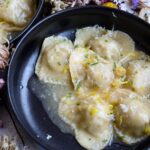 a bowl of ravioli with garnishes of lemon, chives, and cheese