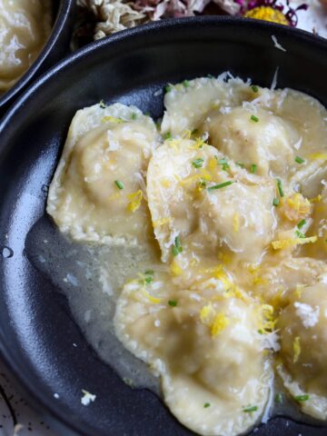 a bowl of ravioli with garnishes of lemon, chives, and cheese