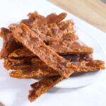 a white plate with strips of vegan jerky stacked in a pile