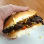 A person holding a vegan philly cheesesteak over a white plate