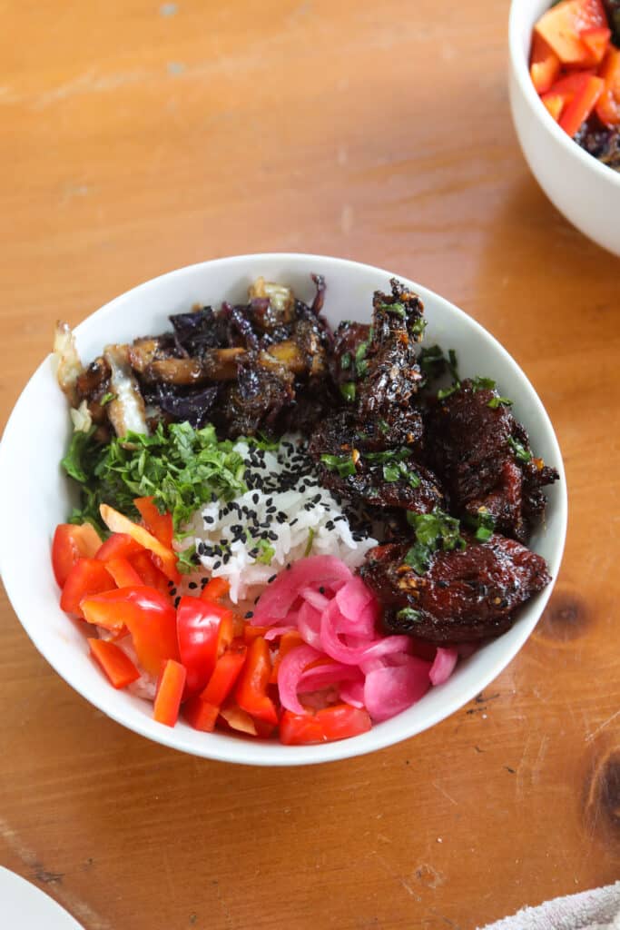 A bowl of fried seitan, stir fried vegetables, with fresh vegetables over white rice